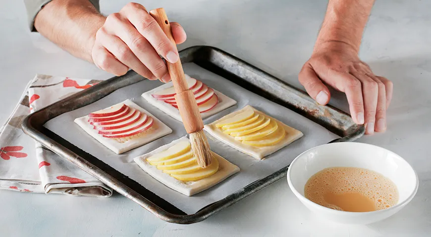 Заготовки слоек с яблоками нужно смазать очень быстро и поскорее отправить в разогретую духовку