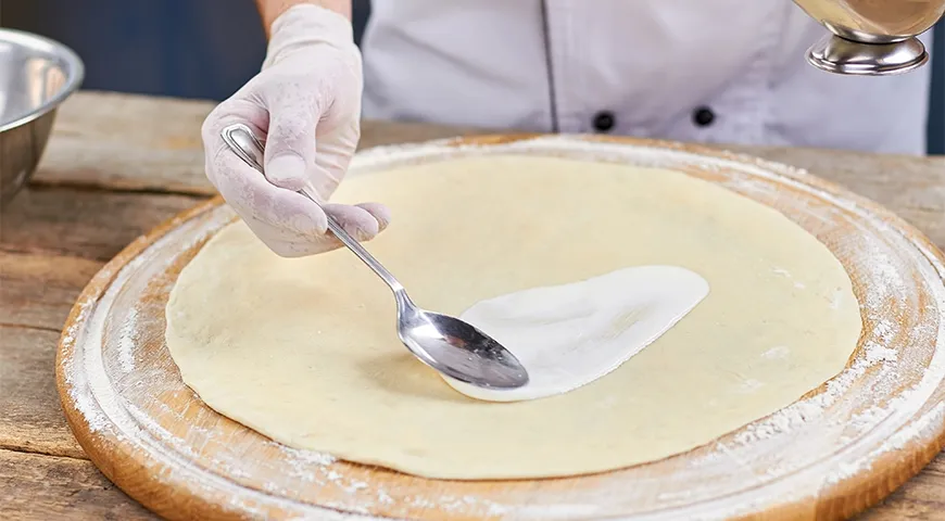 Основу из теста для гавайской пиццы смазывают белым соусом