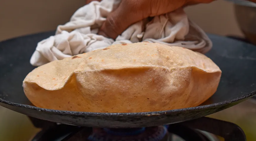 Обжарьте лепешку роти на сухой сковороде по 30 секунд с двух сторон, затем прижмите лепешку лопаткой или чистым полотенцем — она должна вздуться, как шарик