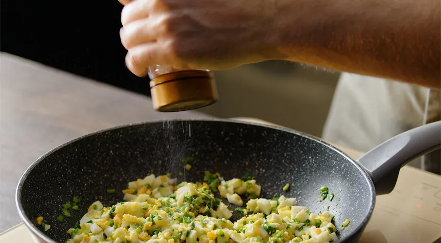 Зеленый лук припустите в сотейнике, добавьте нарезанные яйца, перемешайте, приправьте солью и перцем, остудите