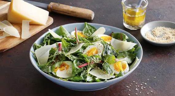 Зеленые салатные листья с сыром, яйцами и кунжутной заправкой