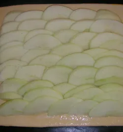 Другую часть теста раскатываем в пласт и выкладываем нарезанные дольки яблок